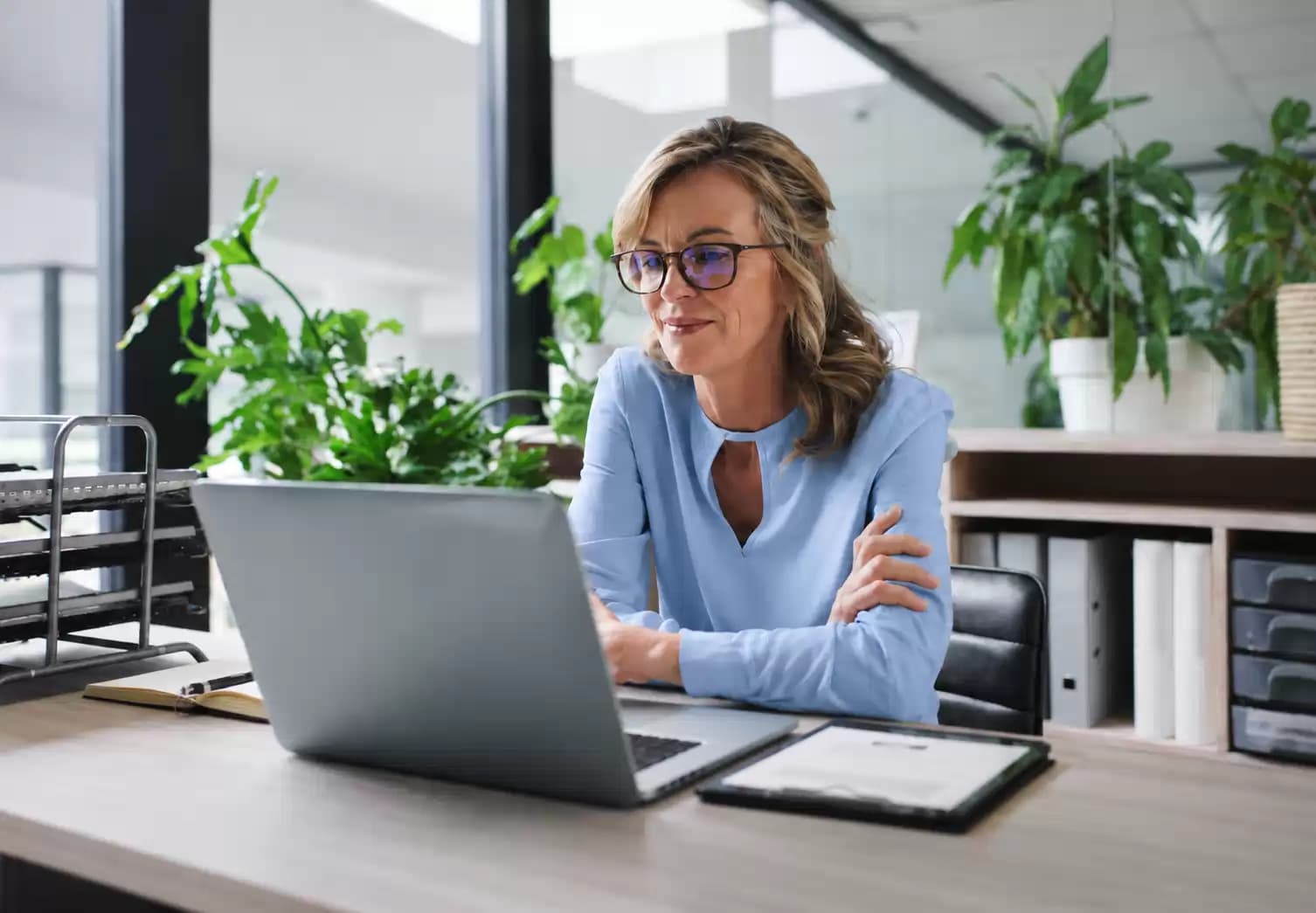 Een vrouw werkt aan een laptop in een lichte kantoorruimte met planten